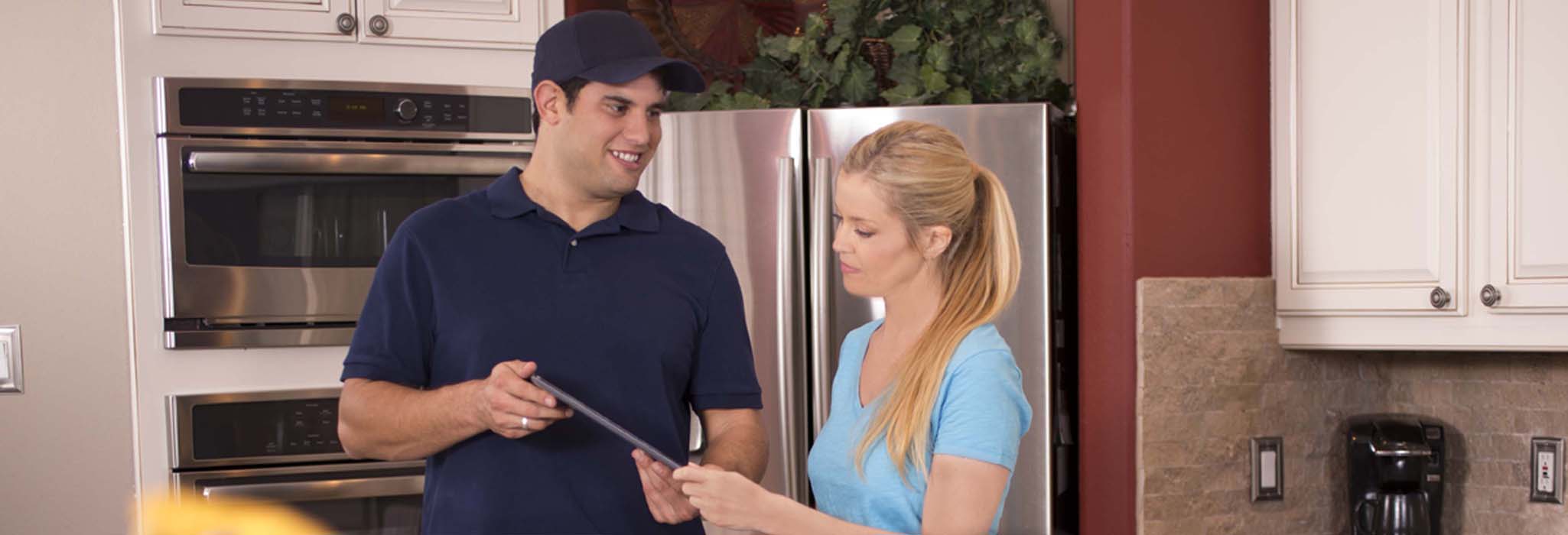 Latin descent repairman or blue collar/service industry worker makes service/house call in customer's home kitchen. Man uses digital tablet to show customer the repair information.  Inspectors, exterminators, plumbers, electricians.  Toolbag foreground.