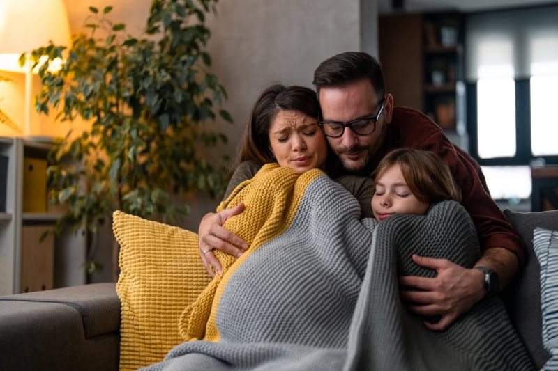 Why Isn’t My Furnace Heating My Entire Home? Family of three, freezing in their home, huddled under a blanket to keep warm.